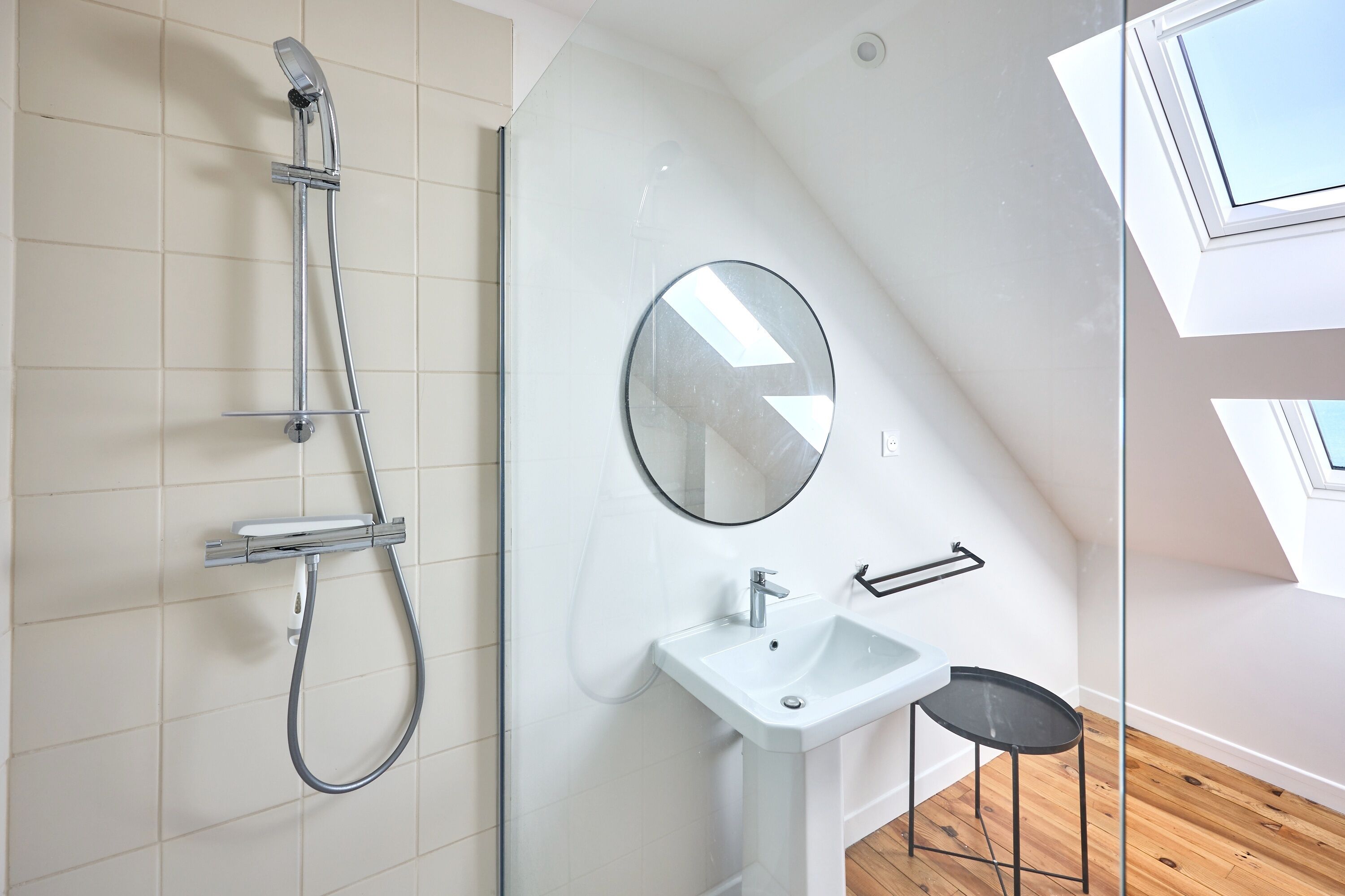 A modern bathroom with a glass shower enclosure, a white sink, and a mirror.