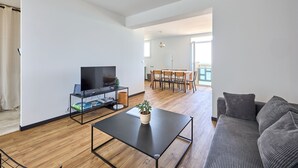 A modern living room with a flat-screen TV, a coffee table with a plant, and a grey sofa.