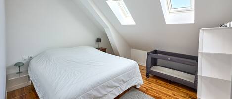 Un dormitorio con cama, cuna, tragaluz y ventana.