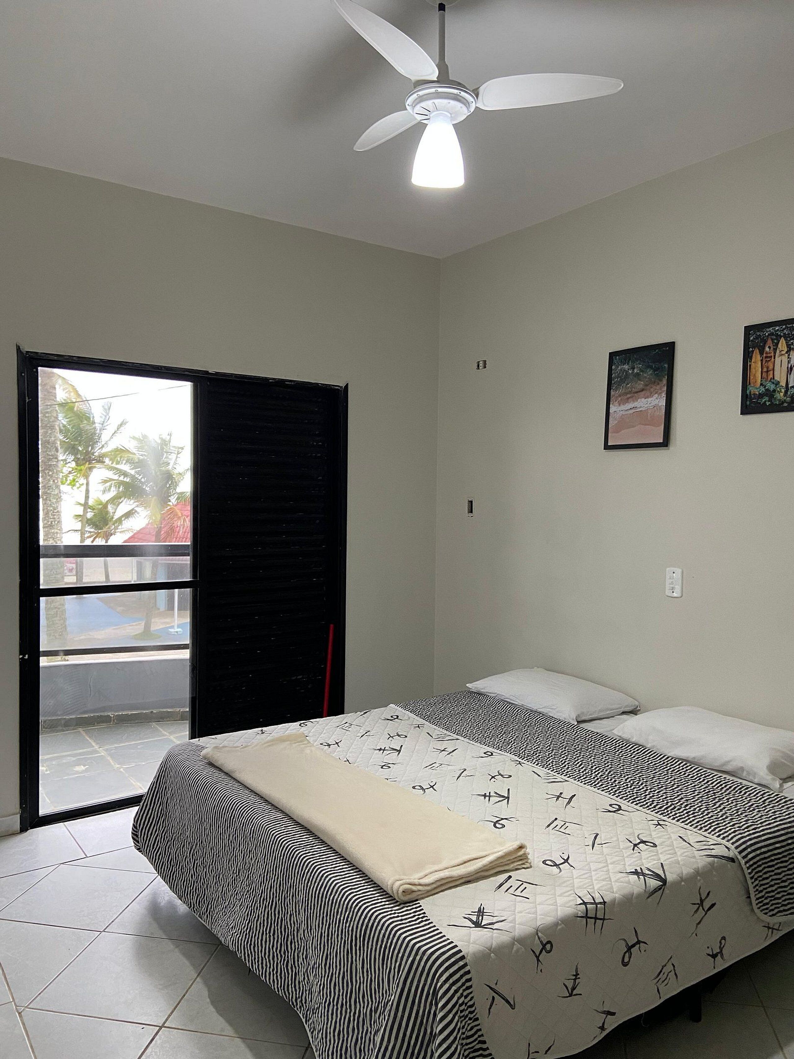 Een slaapkamer met een bed, een plafondventilator, een raam met uitzicht en een deur.
