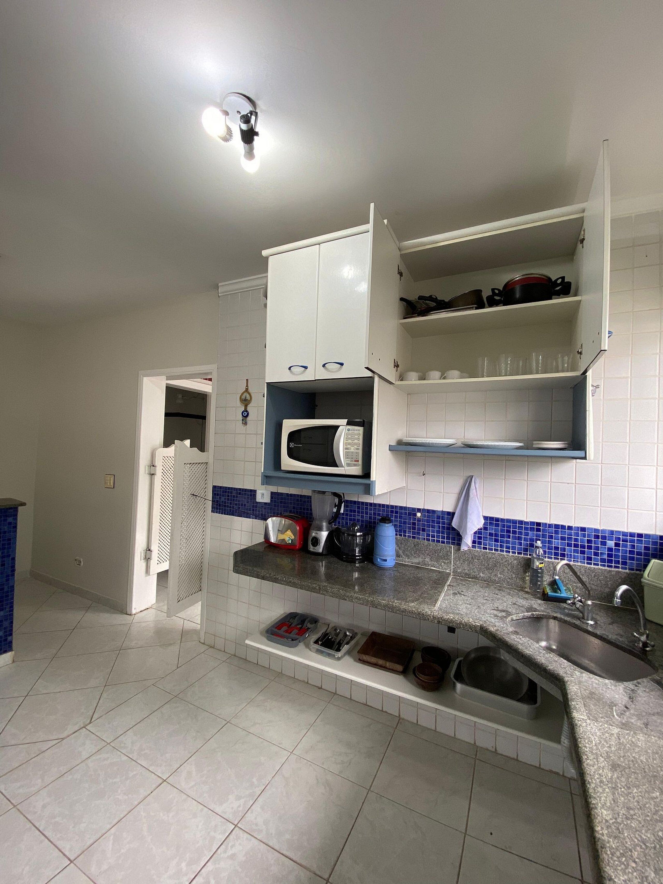 A kitchen with white cabinets, a microwave, a blender, and a sink.