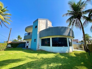 A modern two-story building with a curved balcony, surrounded by well-maintained grass and palm trees.