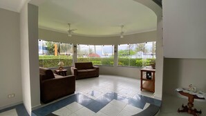 A spacious living area with a curved floor, large windows, and a ceiling fan. - Casa Alto Padrão Frente ao Mar (Peruibe)