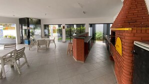 A modern indoor space with a brick oven, seating area, and large windows. - Casa Alto Padrão Frente ao Mar (Peruibe)