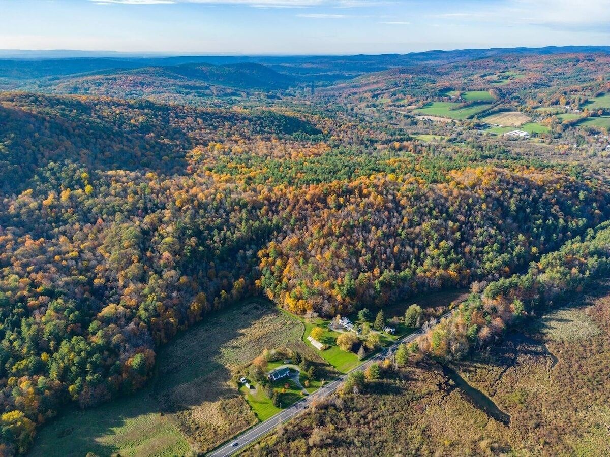 Luchtbeeld van een bebost gebied met een kleine groep gebouwen, waarschijnlijk een resort of lodge, omgeven door herfstkleurige bladeren.