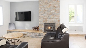A living room with a stone fireplace, leather sofa, and a flat-screen TV mounted on the wall.