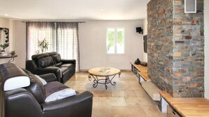 A living room with a stone fireplace, leather sofas, a round coffee table, and a large window with curtains.
