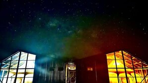 Un edificio con un cielo estrellado visible a través de amplios ventanales, una puerta central e interior muy iluminado.