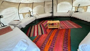 Un alojamiento en tienda de campaña con varias camas, una mesa de madera en el centro y alfombras de colores.