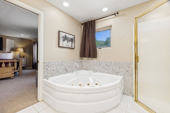 A bathroom with a large white bathtub, a small window with a view, and a framed picture on the wall. - Eagles Nest at Creekside on the 17th Green! (Estes Park)