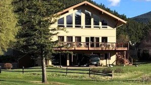 A two-story building with a balcony, surrounded by a fenced yard and a mountain backdrop.