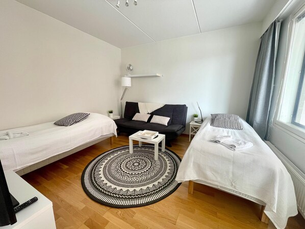 Una habitación compacta y bien iluminada con dos camas individuales, un sofá, una mesita y un tapete estampado.