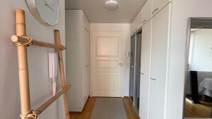 Un pasillo con suelo de madera, un tapete estampado, una puerta blanca y un reloj en la pared.