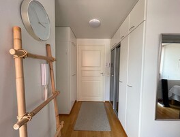 Käytävä, jossa on puulattia, kuviollinen matto, valkoinen ovi ja seinällä oleva kello.