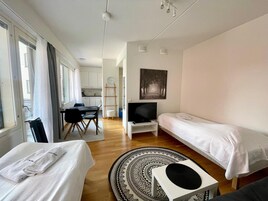 Kompakti hotellihuone, jossa on sänky, televisio, työpöytä tuolilla ja taaempana keittiöalue.