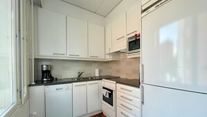 Una cocina compacta con armarios blancos, horno integrado, microondas y lavavajillas.