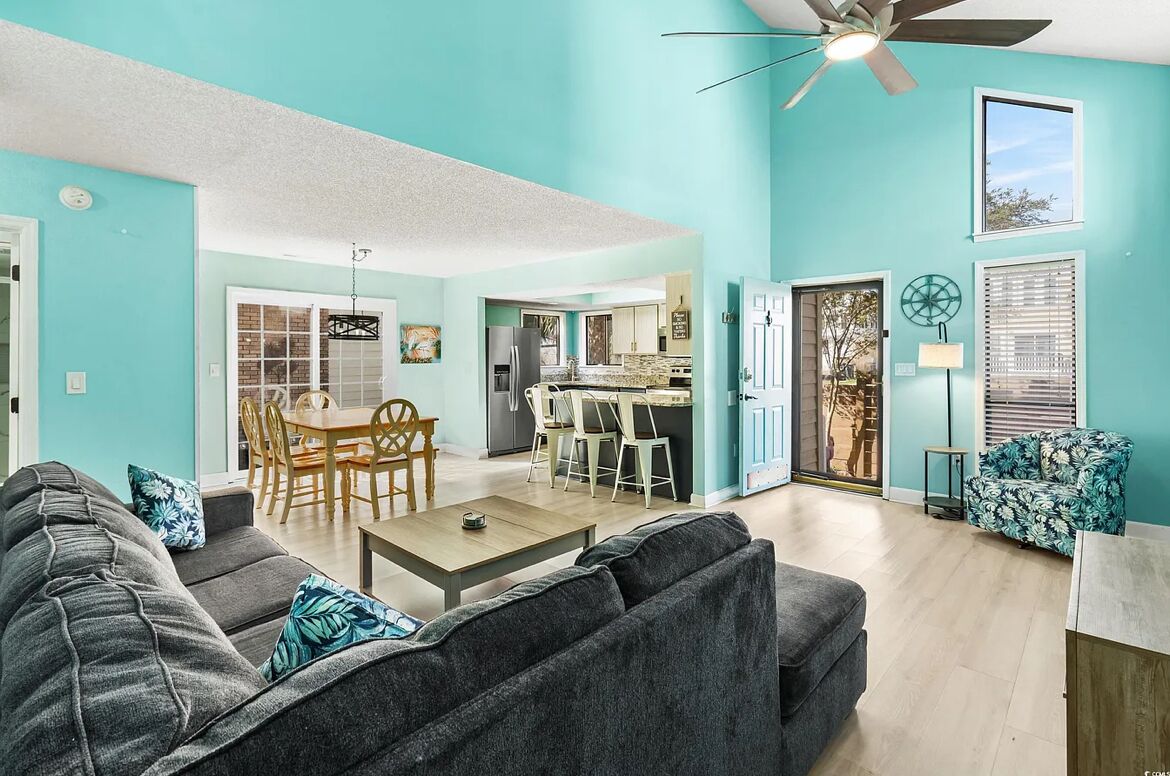 A spacious living area with a dining table, a sofa, and a ceiling fan.
