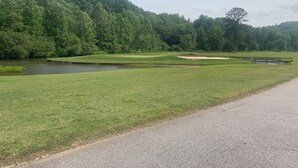 A golf course with a pond, a sandy area, and a road alongside.