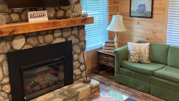 A cozy living room with a stone fireplace, a green sofa, and a colorful rug.