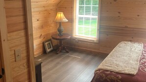 A wooden room with a bed, a lamp, a window, and a small table.