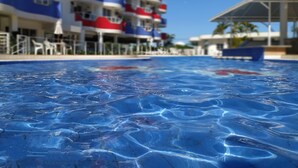A swimming pool with a clear blue water surface, surrounded by a multi-story hotel building with balconies.