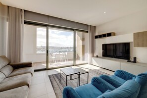 Relax in a spacious living room with a large sliding door leading to a balcony offering a city view, a flat-screen TV, and a comfortable seating area.