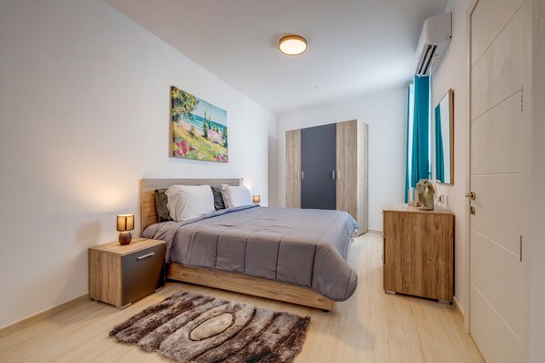 Un dormitorio moderno con cama, mesitas de noche, cómoda, un cuadro y un equipo de aire acondicionado.