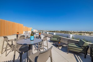 Una terraza en la azotea con una mesa, sillas y una botella de vino.