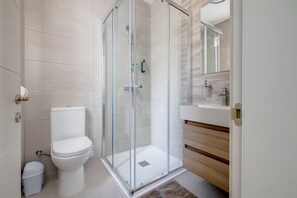 Un baño moderno con ducha envuelta en vidrio, inodoro blanco y tocador de madera con espejo.