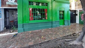 Um edifício verde com janela e porta, uma placa com a inscrição "Hostal Motoposada" e uma árvore em primeiro plano.