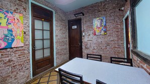Quarto com parede de tijolos, porta de madeira, uma mesa e cadeiras.