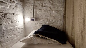 Quarto com cama em frente a uma parede texturizada, luminária e termostato.