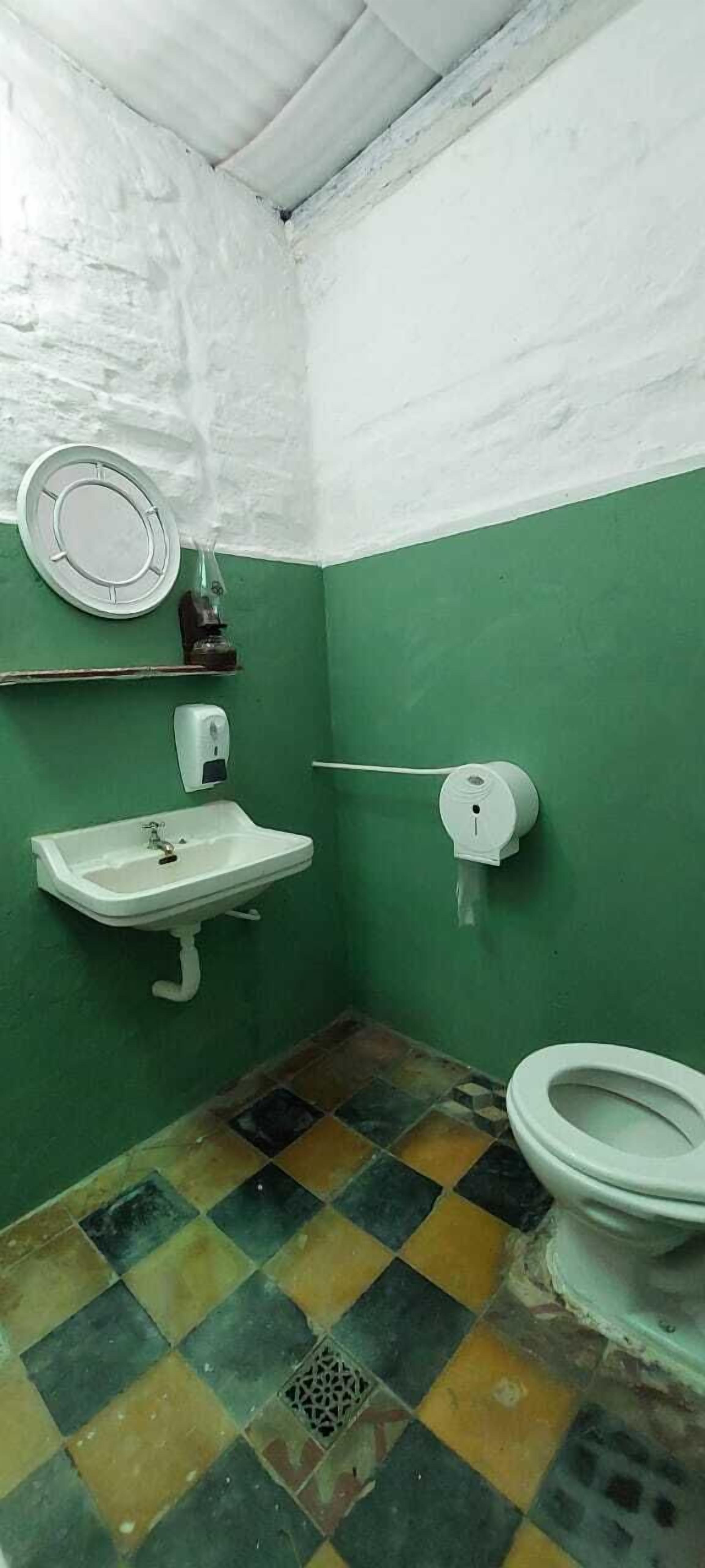 Et lille badeværelse med grønne og hvide farver, en hvid vask, et toilet og et spejl på væggen.