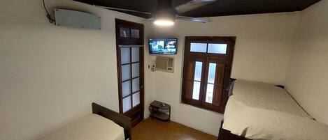 A small room with two beds, a television on the wall, and a ceiling fan.