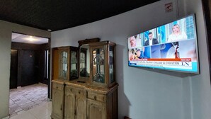 Quarto com um armário de madeira e uma televisão exibindo um canal de notícias.