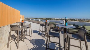 A rooftop terrace with outdoor seating, a bottle of wine, and a view of the city.