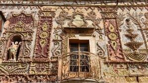 A building facade with intricate carvings, a statue, and a window with ornate ironwork.