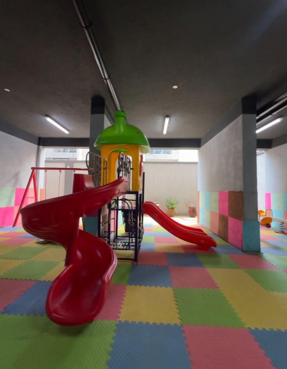 Espaço de recreação com dois escorregadores vermelhos e uma estrutura de escalada verde.