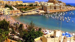 A coastal town with a marina filled with boats, a sandy beach, and buildings with balconies overlooking the water. - Spacious 3BR Residence by the Promenade (Gzira)