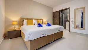 A modern hotel room with a large bed, a bedside table with a lamp, a mirror, and a shower area.