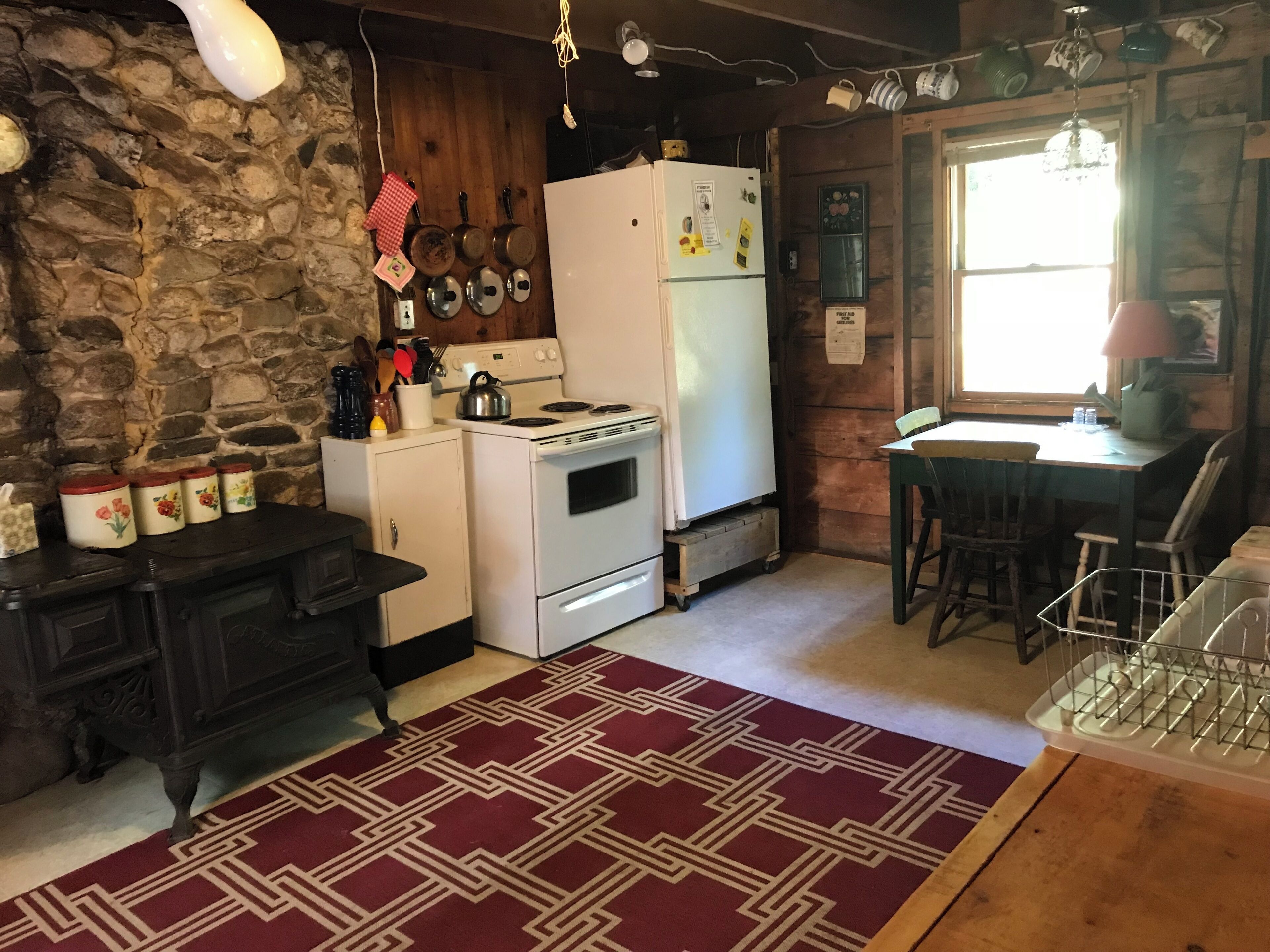 Una cocina rústica con pared de piedra, armarios de madera, una estufa, un refrigerador y un comedor con mesa y sillas.