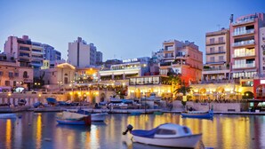 A waterfront area with boats docked, a building with 'DOLCE VITA' signage, and a row of brightly lit establishments along the shore. - Chic 2BR Penthouse Steps from the Waterfront (Gzira)