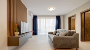 A modern living room with a grey sofa, a flat-screen TV, and a potted plant. - Seaside Escape, Spacious 3BR Bugibba (Saint Paul's Bay)