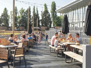Een terras met houten tafels en banken, omgeven door een houten terras en lichtjes.