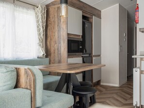 Cocina compacta con microondas, horno y refrigerador. Hay una mesa de madera con dos sillas y un sofá con un cojín.