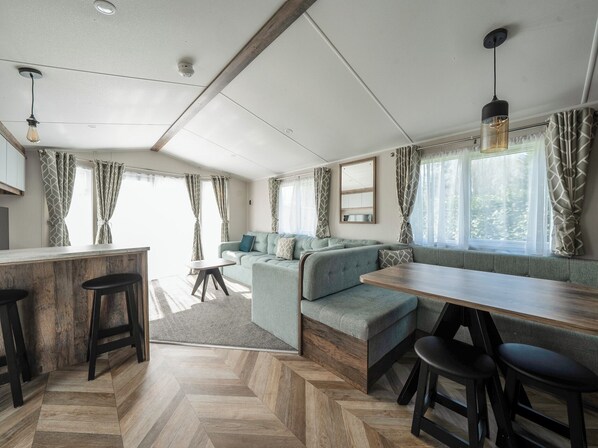 Interior moderno de una caravana, con zona de cocina, asientos y ventanas amplias.