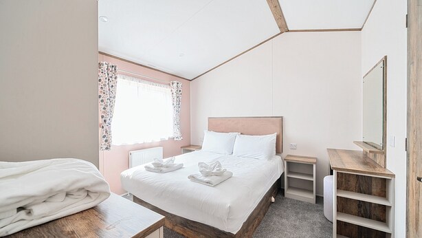 A neatly arranged bedroom with a bed, bedside tables, a mirror, and a wooden shelf unit. - Aquadrome Abode - Billing Aquadrome (Northampton)