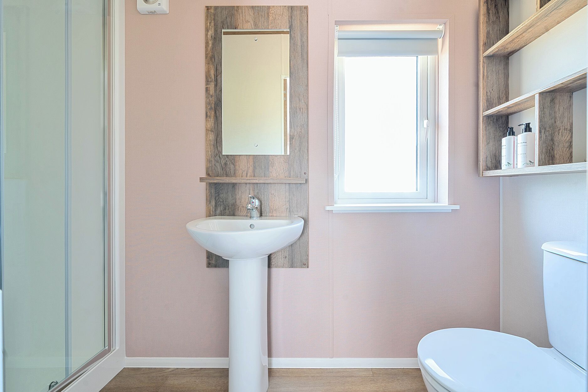 A bathroom with a white sink, a mirror, a window, and a toilet.