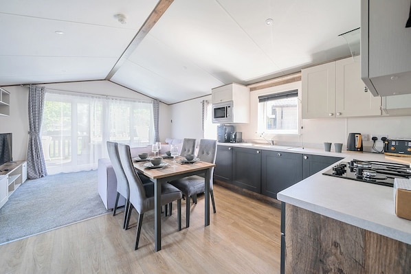 Una cocina compacta con electrodomésticos modernos, un comedor con mesa y sillas, y vistas al exterior a través de amplios ventanales.