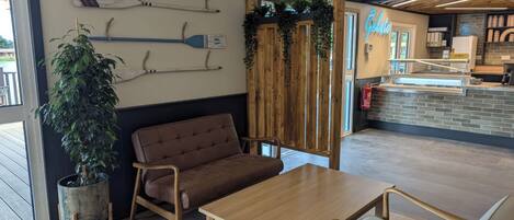 A modern interior with a wooden table, cushioned seating, a potted plant, and a wall-mounted paddleboard.